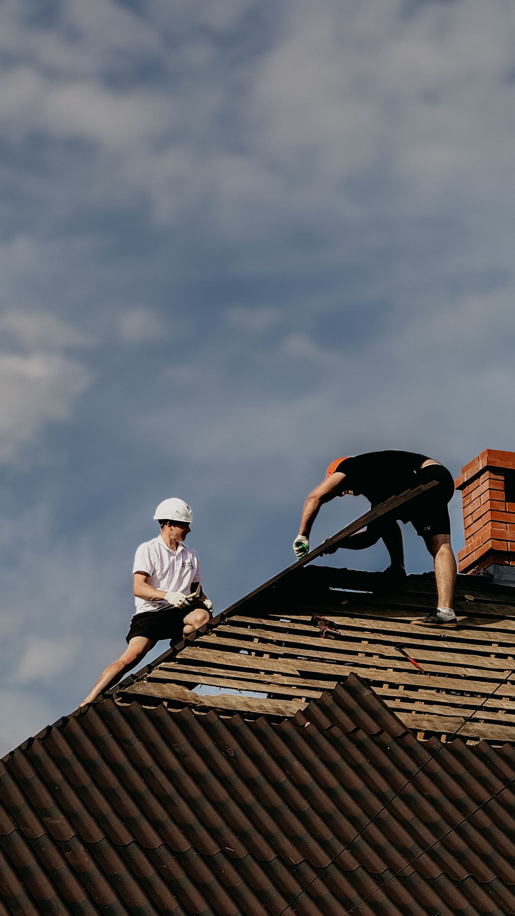 Two roofers in harnesses working together along a shingle roof ridge