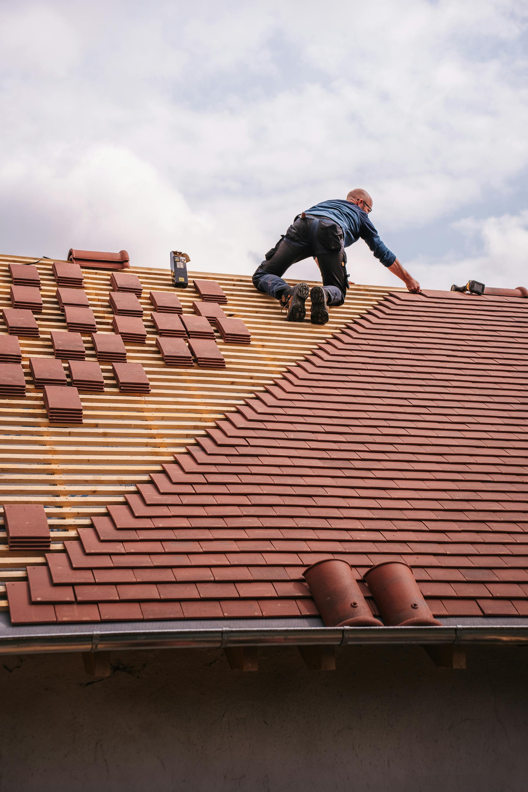 Roofer in harness nailing architectural shingles on a steep residential roof